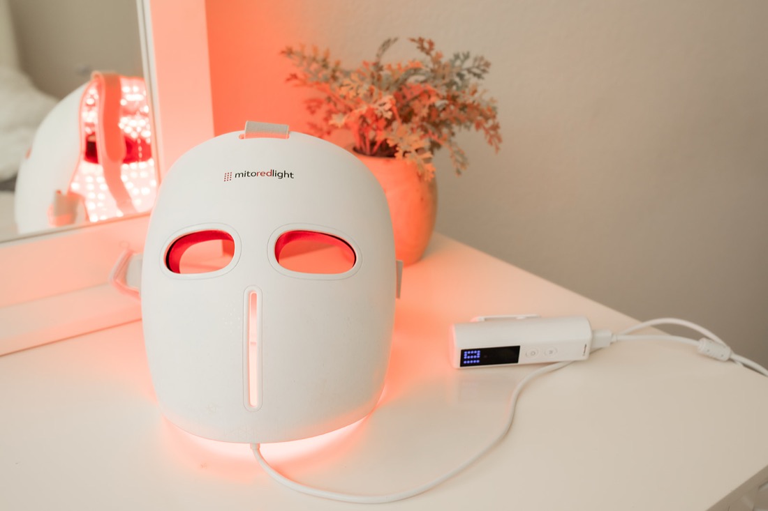 MitoGLOW LED face mask glowing red on a vanity with its controller